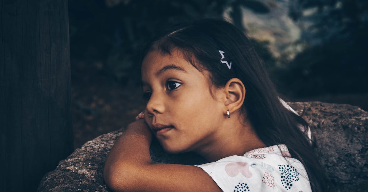 a-little-girl-is-sitting-on-a-rock-looking-at-something