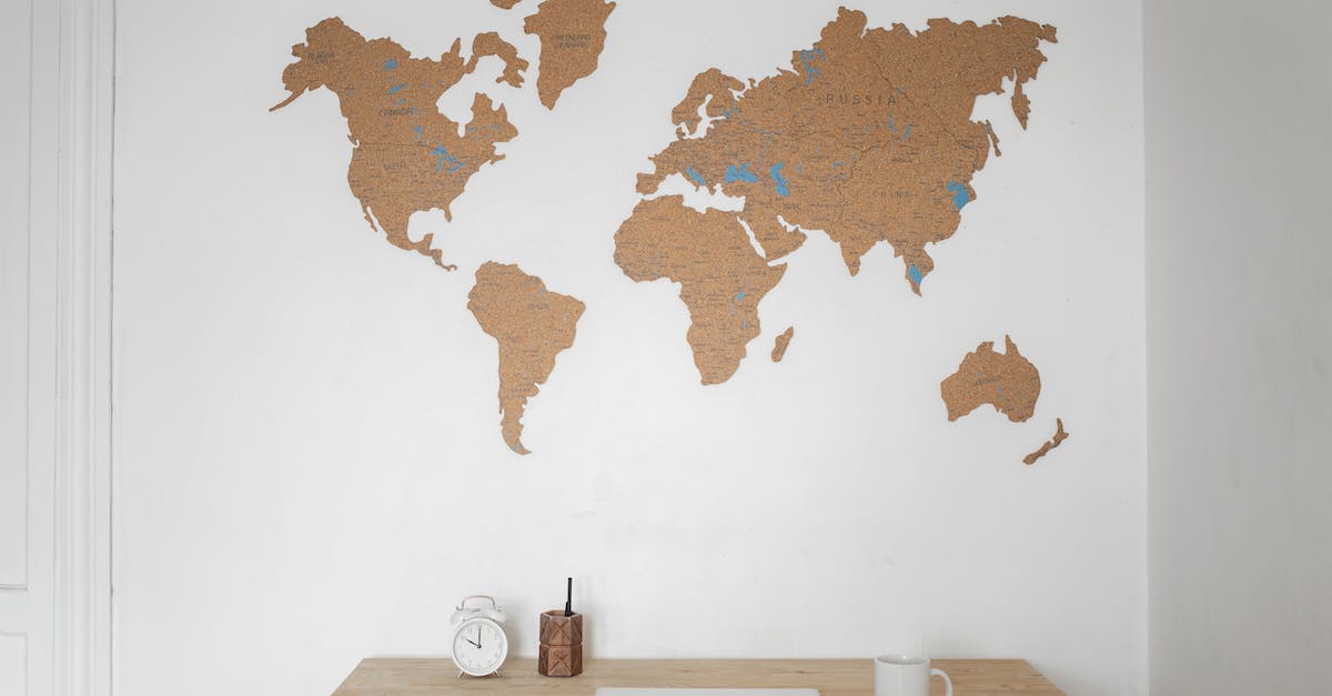 alarm-clock-near-pen-container-with-cup-and-laptop-on-table-placed-near-silhouettes-of-world-map-on