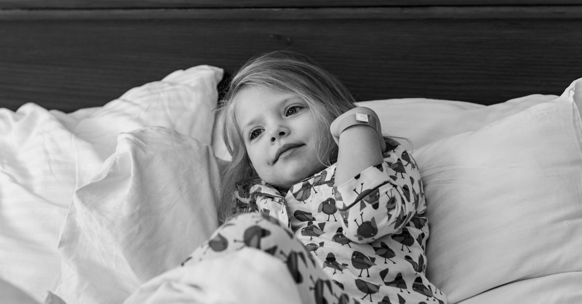 black-and-white-of-adorable-little-girl-in-pajama-lying-on-bed-with-soft-pillows-and-looking-away-in