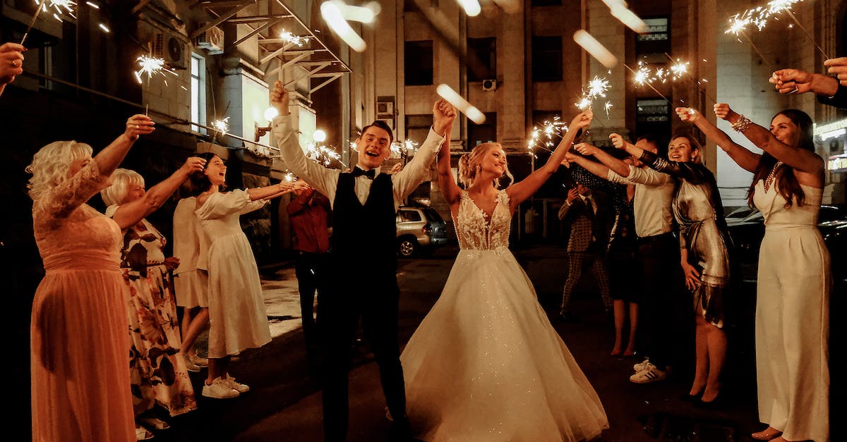 cheerful-young-bride-and-groom-with-guests-dancing-on-street-with-sparklers-in-hands-during-wedding