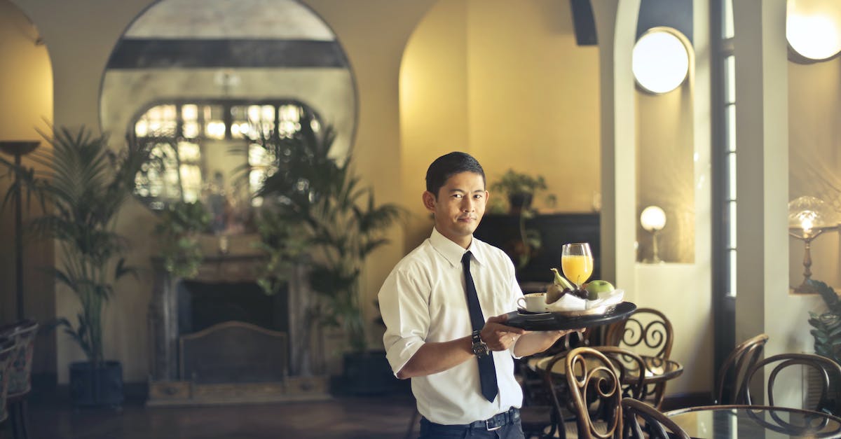confident-young-ethnic-waiter-in-elegant-clothes-holding-tray-with-food-and-drinks-and-looking-at-ca