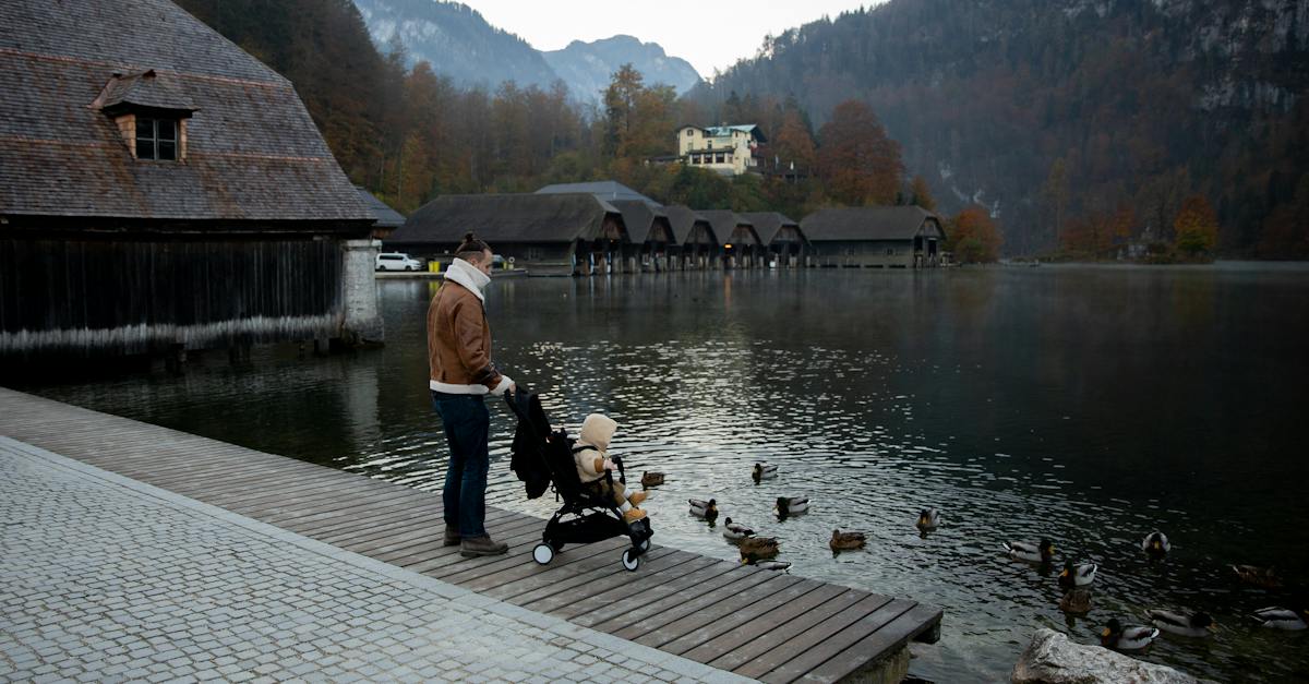 father-and-little-kid-in-stroller-in-casual-warm-outerwear-standing-on-wooden-pier-near-lake-and-lo
