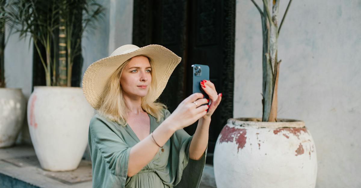 female-tourist-wearing-summer-dress-and-broad-brim-hat-taking-photo-on-cellphone-white-standing-on-s