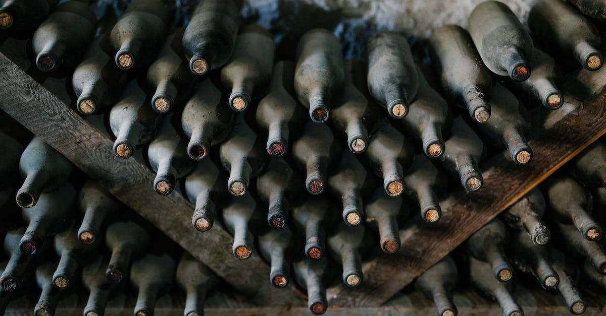 from-above-of-dusty-bottles-of-alcohol-drink-placed-above-each-other-in-rows-in-winery