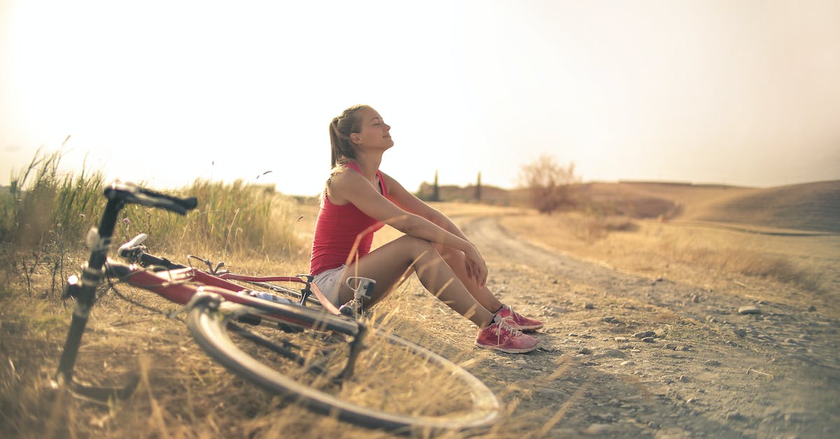 full-body-of-female-in-shorts-and-top-sitting-on-roadside-in-rural-field-with-bicycle-near-and-enjoy