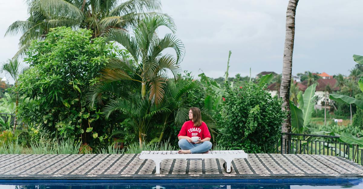 lady-in-red-sweatshirt-and-blue-jeans-sitting-alone-near-empty-swimming-pool-with-white-mug-bowl-of
