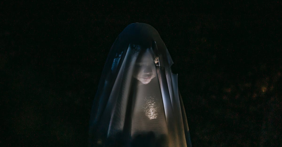 mysterious-little-girl-standing-in-darkness-covered-with-white-blanket-as-ghost-and-shining-flashlig