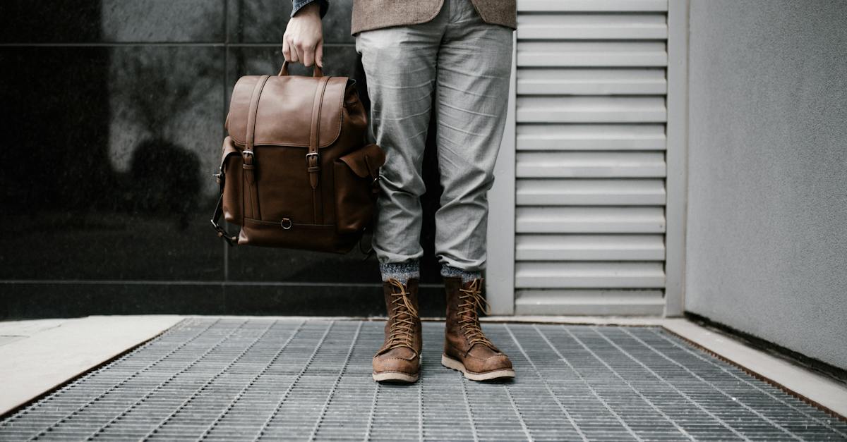 photo-of-man-in-brown-blazer-gray-pants-and-brown-boots-holding-brown-leather-bag-standing-outside
