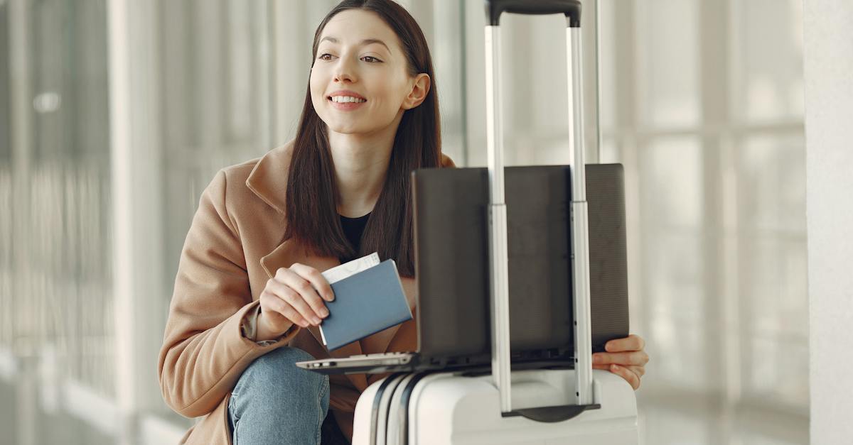 positive-woman-with-passport-using-laptop-on-luggage-in-airport