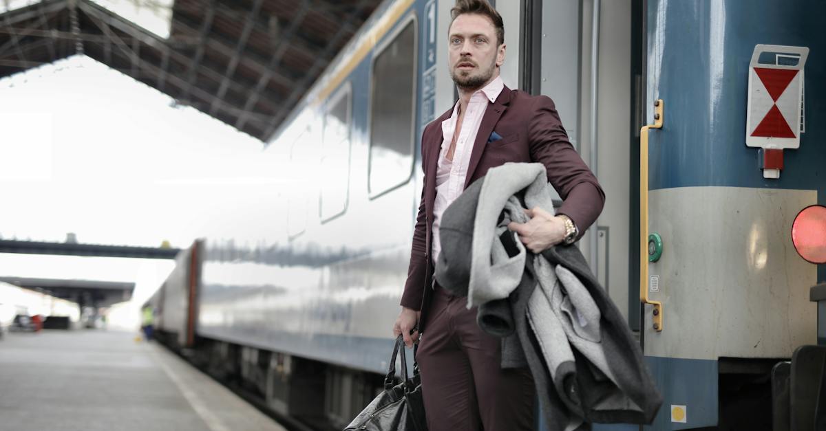 serious-stylish-bearded-businessman-in-trendy-suit-holding-bag-and-coat-in-hands-standing-near-train