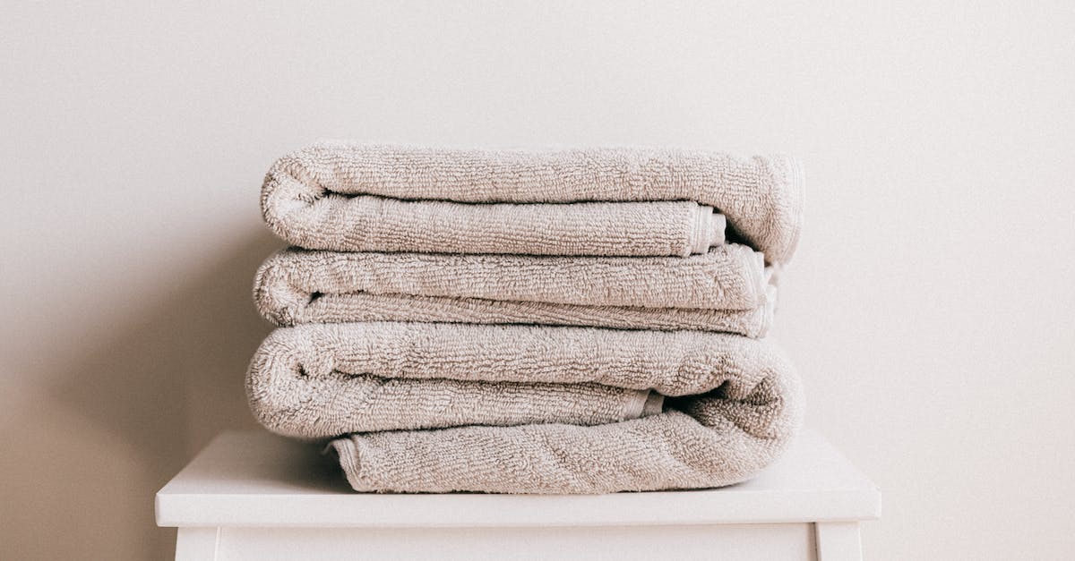 stack-of-soft-clean-light-beige-folded-towels-placed-on-white-minimalist-stool-against-beige-wall-in