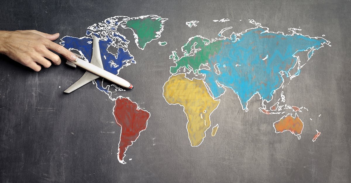 top-view-of-crop-anonymous-person-holding-toy-airplane-on-colorful-world-map-drawn-on-chalkboard-1