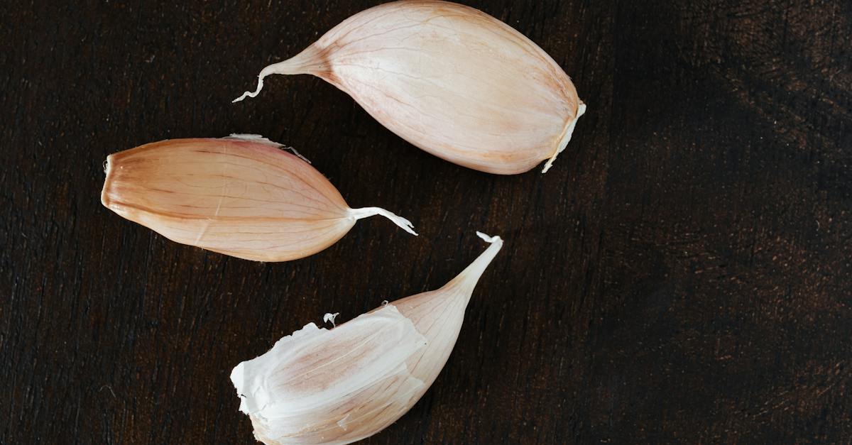 top-view-of-several-cloves-of-ripe-garlic-in-peel-placed-on-wooden-desk-during-cooking-process-at-ho