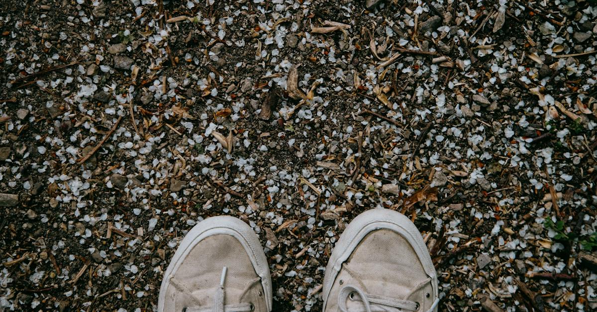 top-view-of-unrecognizable-traveler-in-simple-beige-sneakers-on-ground-covered-with-tiny-stones-and