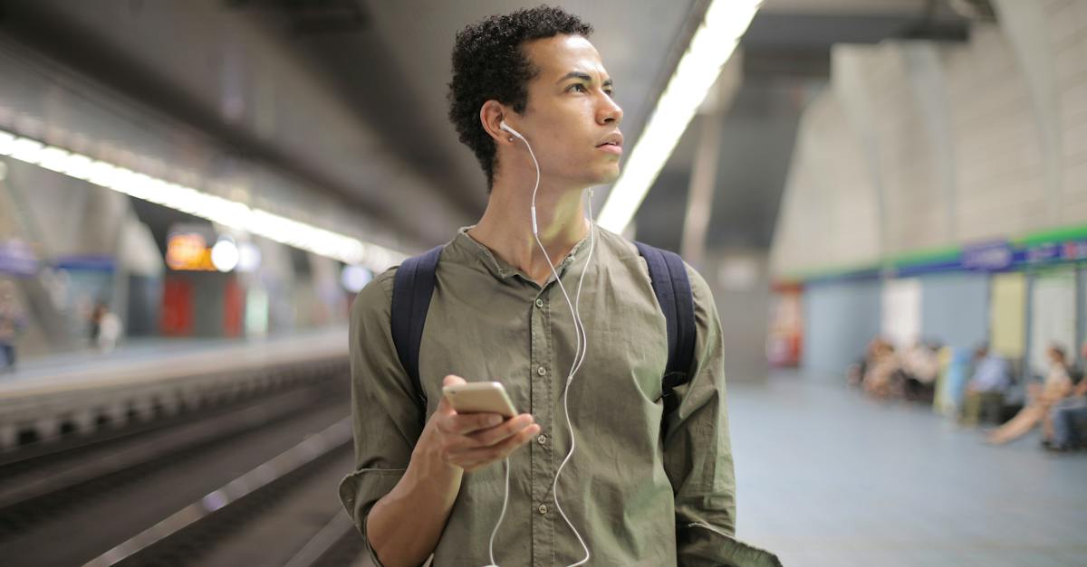 young-ethnic-man-in-earbuds-listening-to-music-while-waiting-for-transport-at-contemporary-subway-st