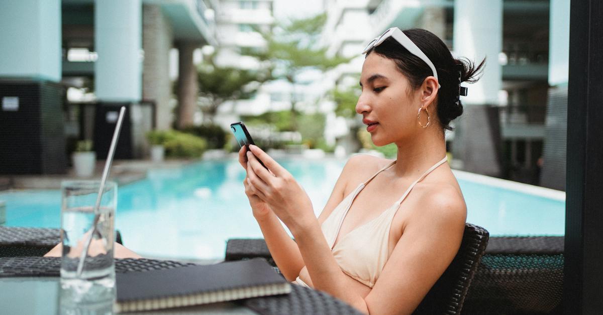 young-ethnic-woman-messaging-on-smartphone-while-chilling-in-cafe-near-outdoor-pool
